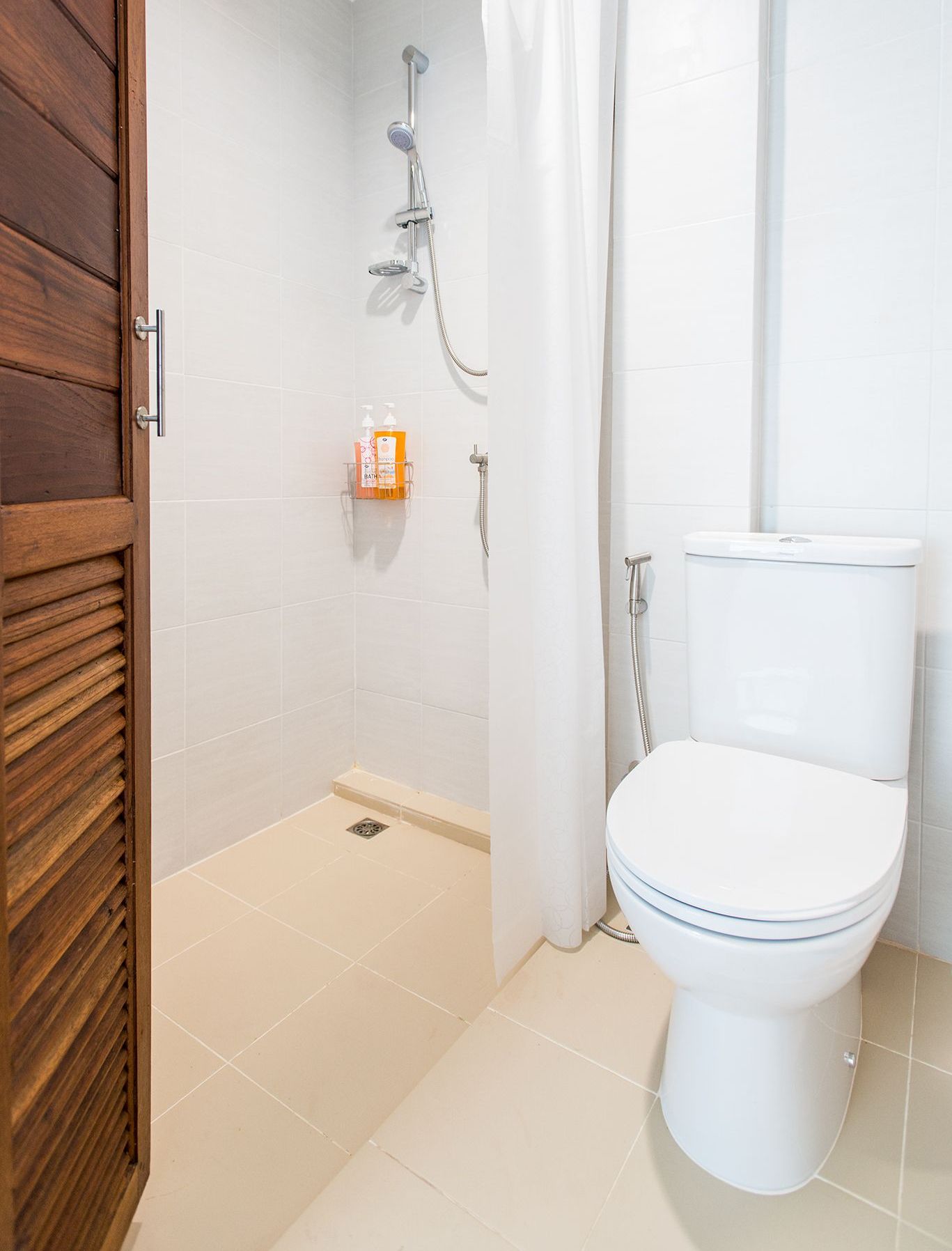 A bathroom with a white toilet, a shower with a curtain, and a wooden door.