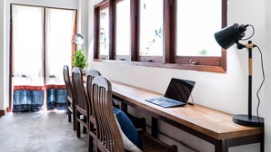 A room with a wooden desk, a laptop, and a lamp. There are chairs and a plant. - Baan Heart Thai - Hostel (Chiang Mai)