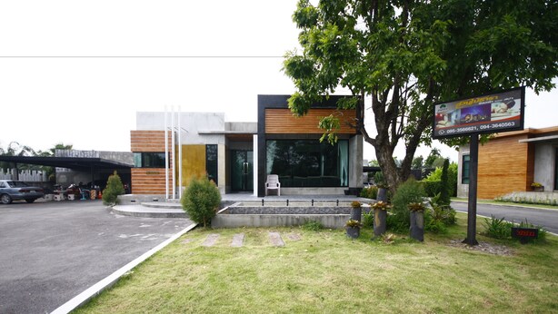 Um edifício moderno com entrada coberta, área gramada com plantas pequenas e uma placa.