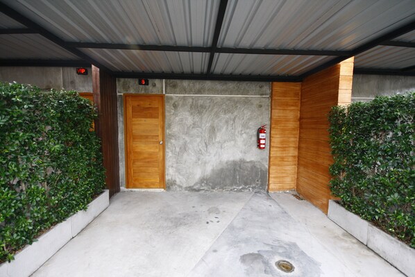 A covered entrance with two wooden doors, a fire extinguisher, and a concrete floor.