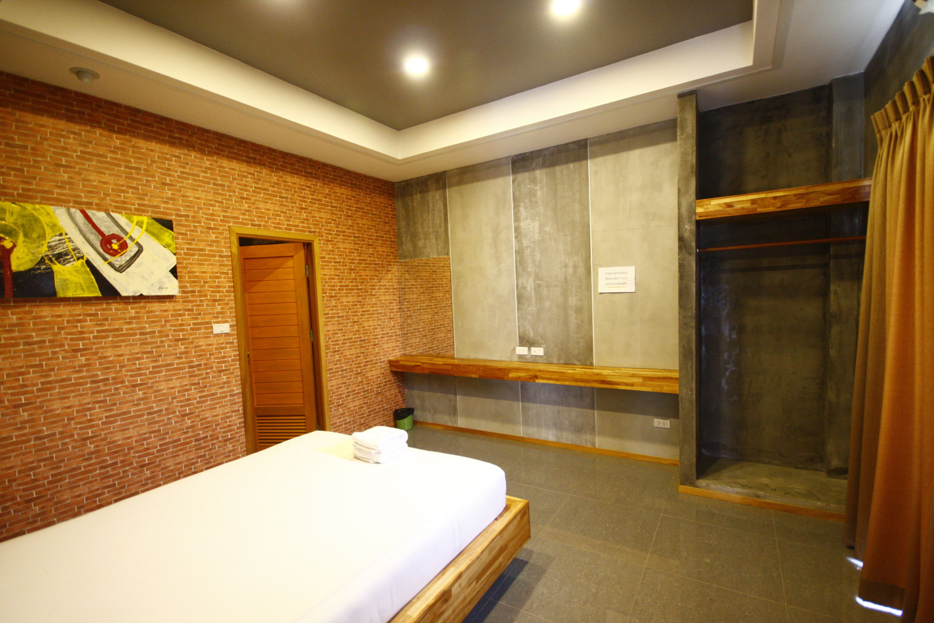 A hotel room with a brick wall, a wooden bed, a shower area, and a bench.