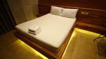 Un lit bien fait, avec du linge de lit blanc et une serviette pliée, une tête de lit en bois et un plancher en bois.