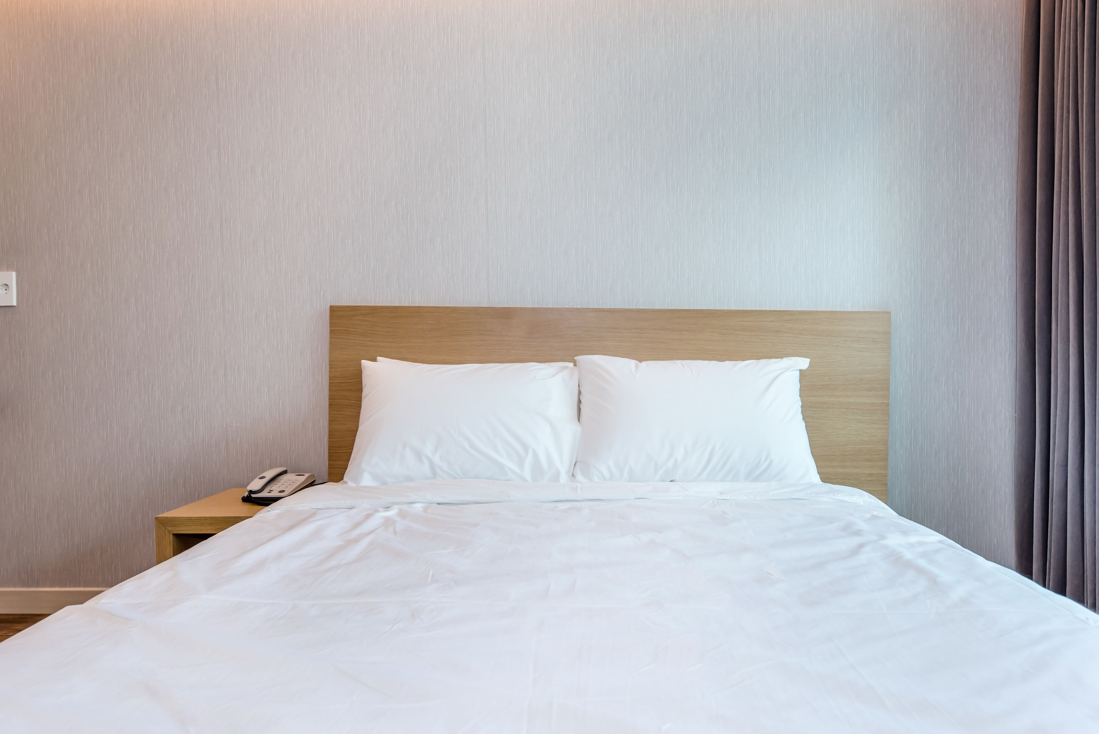 A neatly made bed with white linens, a wooden headboard, and a bedside table with a telephone.
