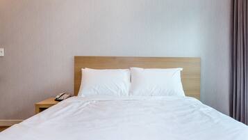 A neatly made bed with white linens, a wooden headboard, and a bedside table with a telephone.