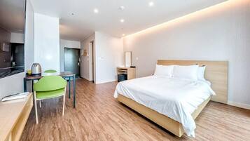 A modern hotel room with a wooden floor, a bed with white linens, a desk with a chair, and a small table with a kettle.