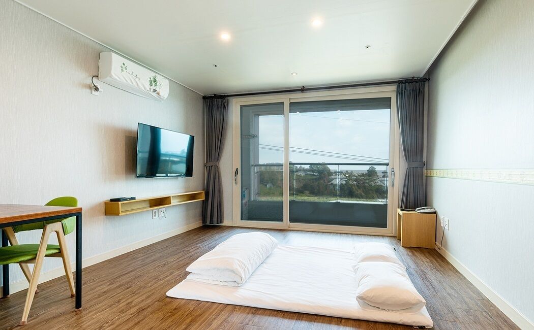 A hotel room with a bed, a TV, a desk with a chair, and a window with curtains.
