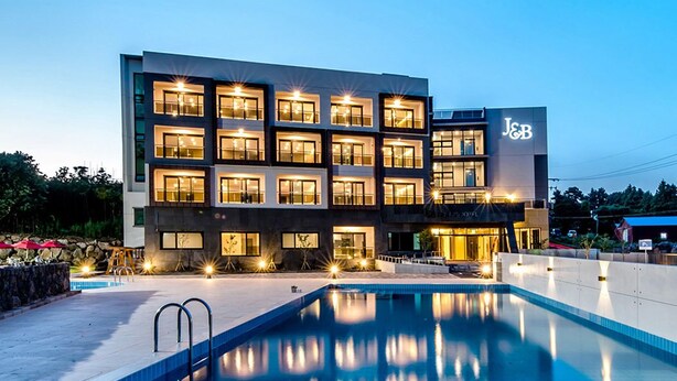 Een modern hotel met meerdere verdiepingen, een zwembad en een goed verlichte gevel.
