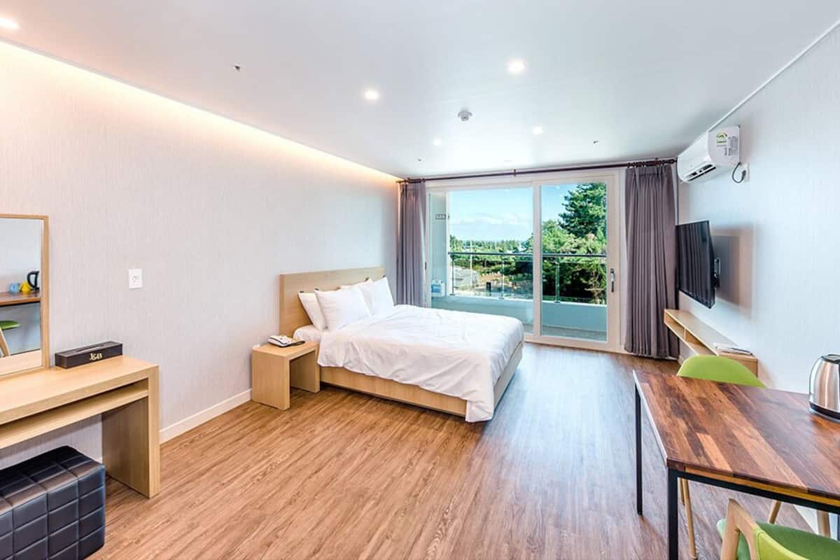 Ein modernes Hotelzimmer mit Bett, Schreibtisch und großem Fenster mit Blick auf Grünflächen.