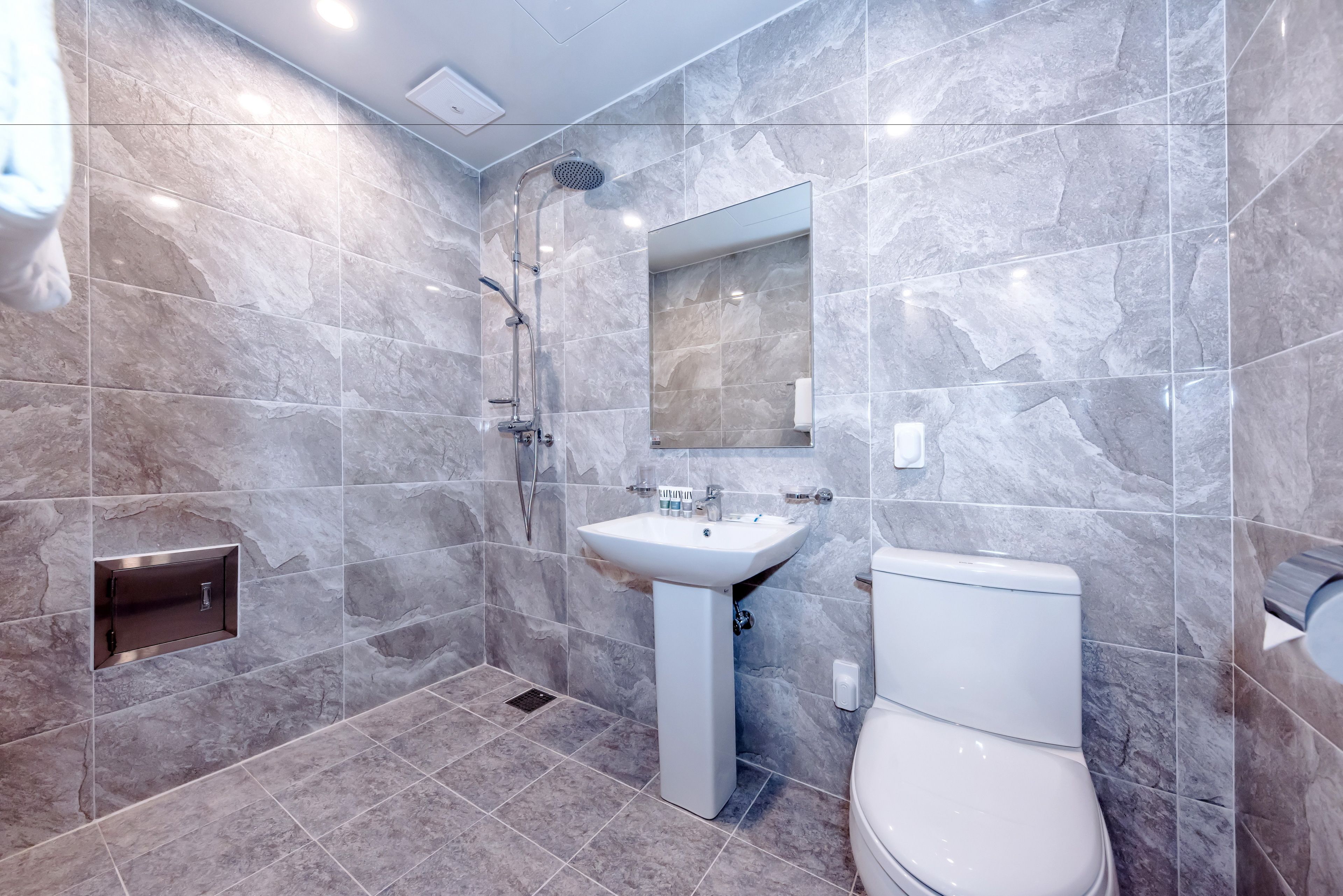 A modern bathroom with a shower, sink, and toilet, featuring marble tiles and a built-in cabinet.