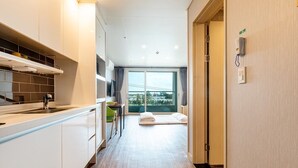 Een moderne hotelkamer met een keukenhoek, een groot raam met uitzicht op de stad, en een bed met uitzicht.