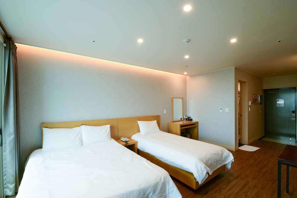 Ein Hotelzimmer mit zwei Betten, einem hölzernen Kopfteil, einem Nachttisch mit Telefon, einem Spiegel und einer Tür zum Badezimmer.