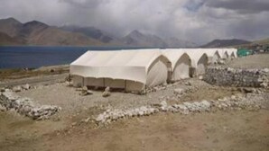 A row of white tents with a mountainous backdrop and a body of water. - The Buddha Camp (Leh)