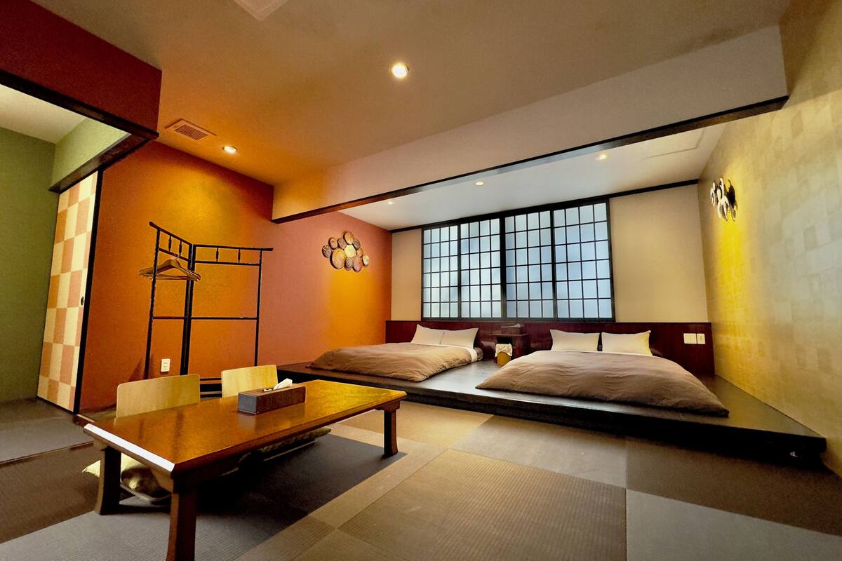A hotel room with a large bed, a small table, a bench, and a window with a view.