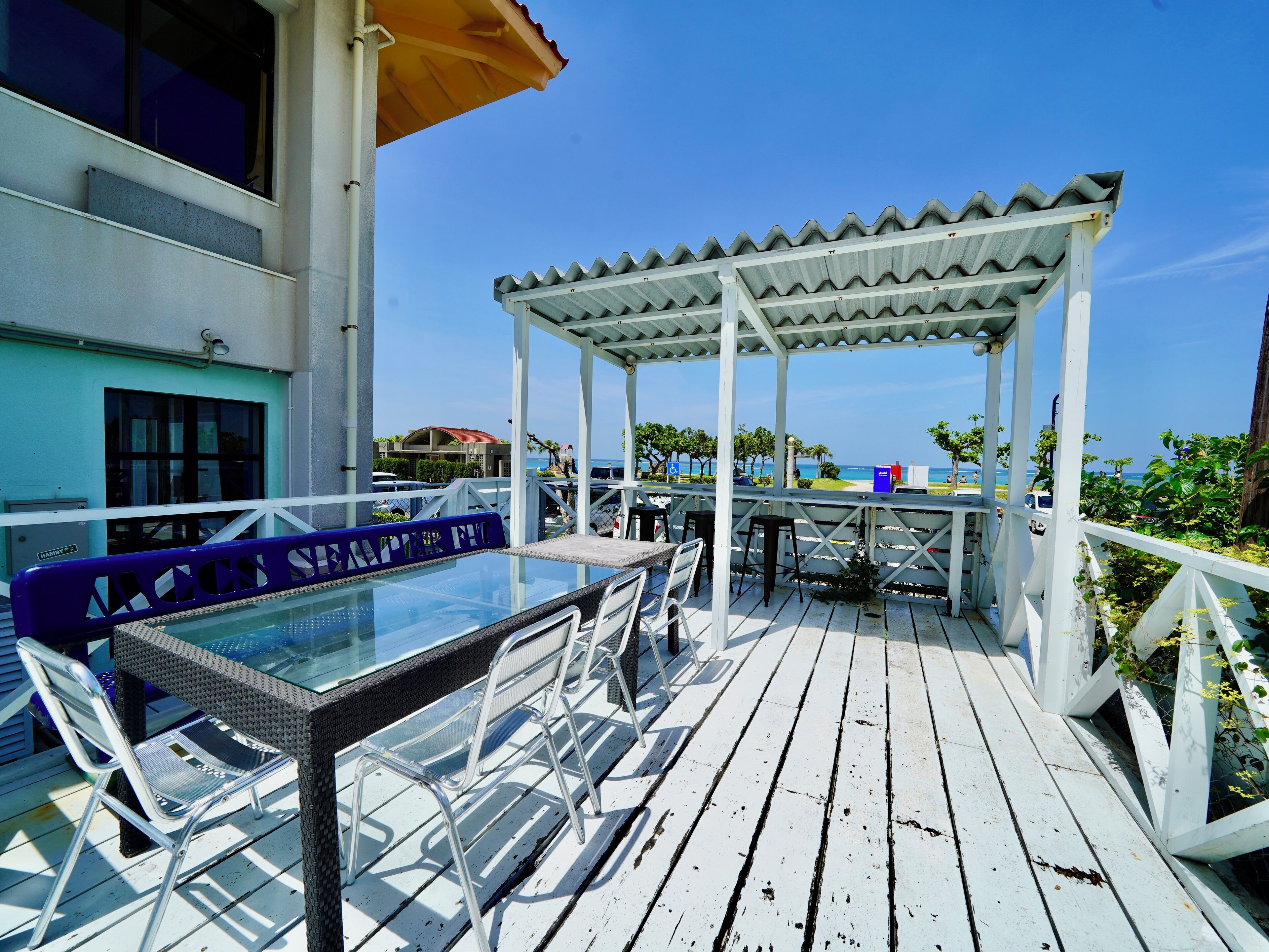 A wooden deck with a glass table and chairs, a covered seating area, and a view of the ocean.