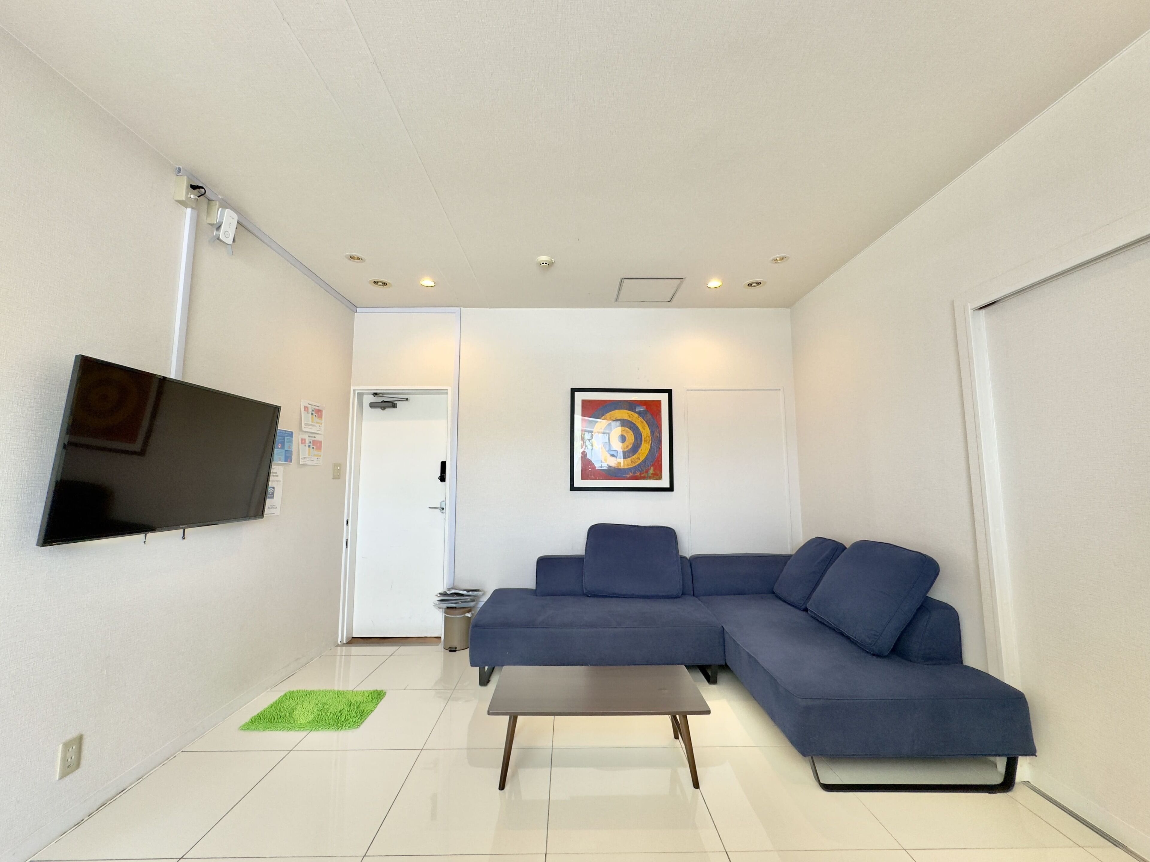 A modern living room with a flat-screen TV, a blue sectional sofa, a small coffee table, and a green rug.