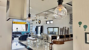 A modern kitchen with a central island, pendant lighting, and a view into the dining area. - Araha Resort ARAPANA (Chatan)