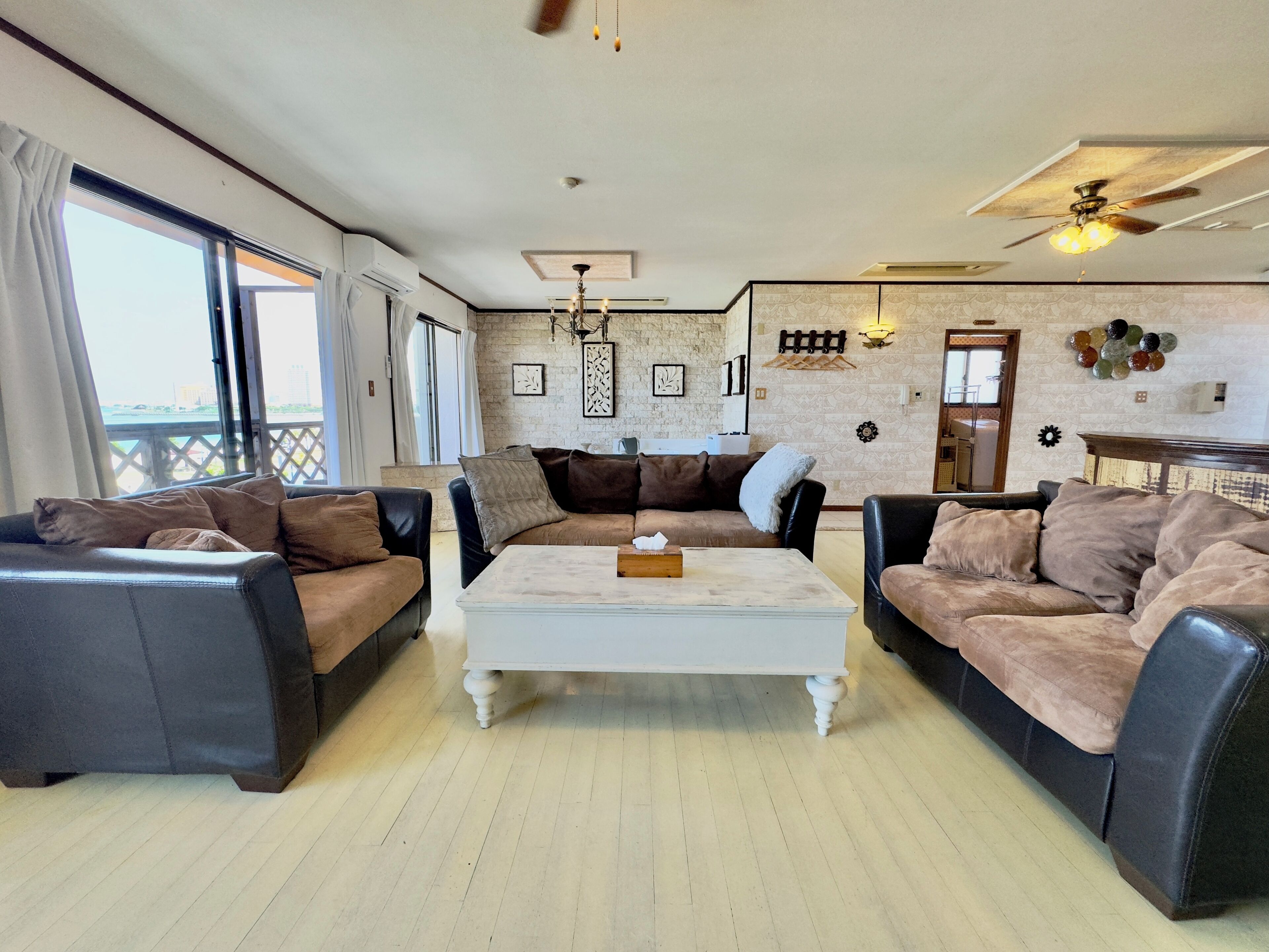 A spacious living room with leather sofas, a white coffee table, and a ceiling fan.