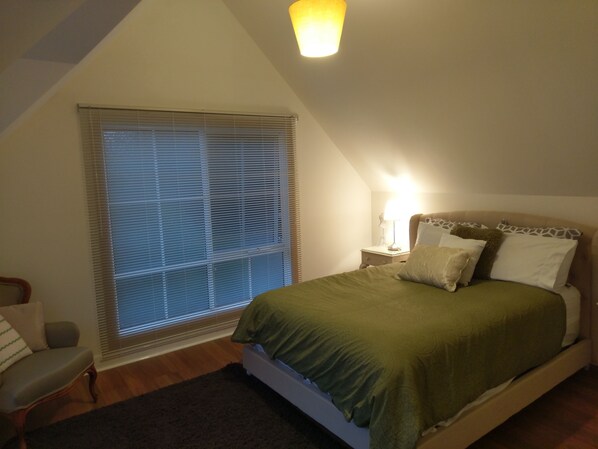 A bedroom with a bed, a nightstand, a lamp, a chair, and a window with blinds. - Malley House (Healesville)