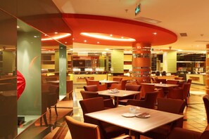 A modern restaurant with multiple dining tables and chairs, a central column, and a bright, warm interior.