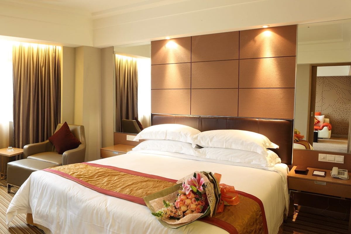 A hotel room with a large bed, a flat-screen TV, a desk with a chair, and a bathroom mirror.