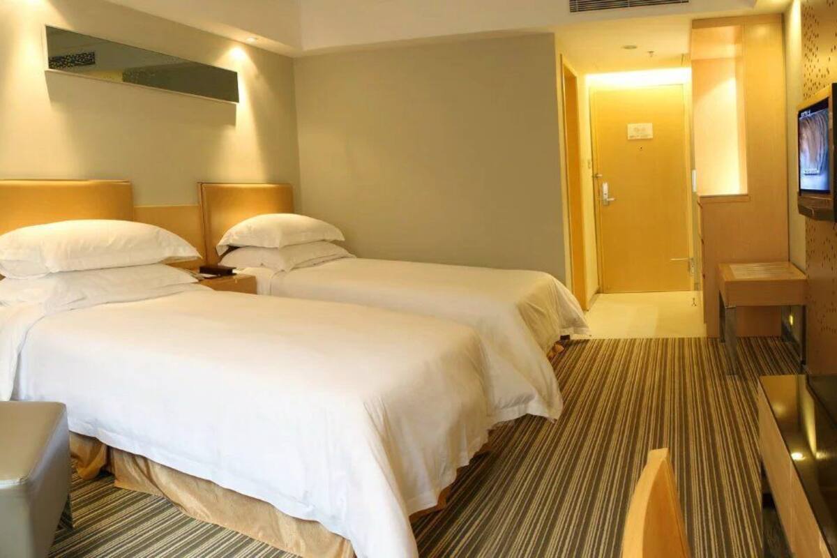 A hotel room with two beds, a desk, a chair, and a TV.