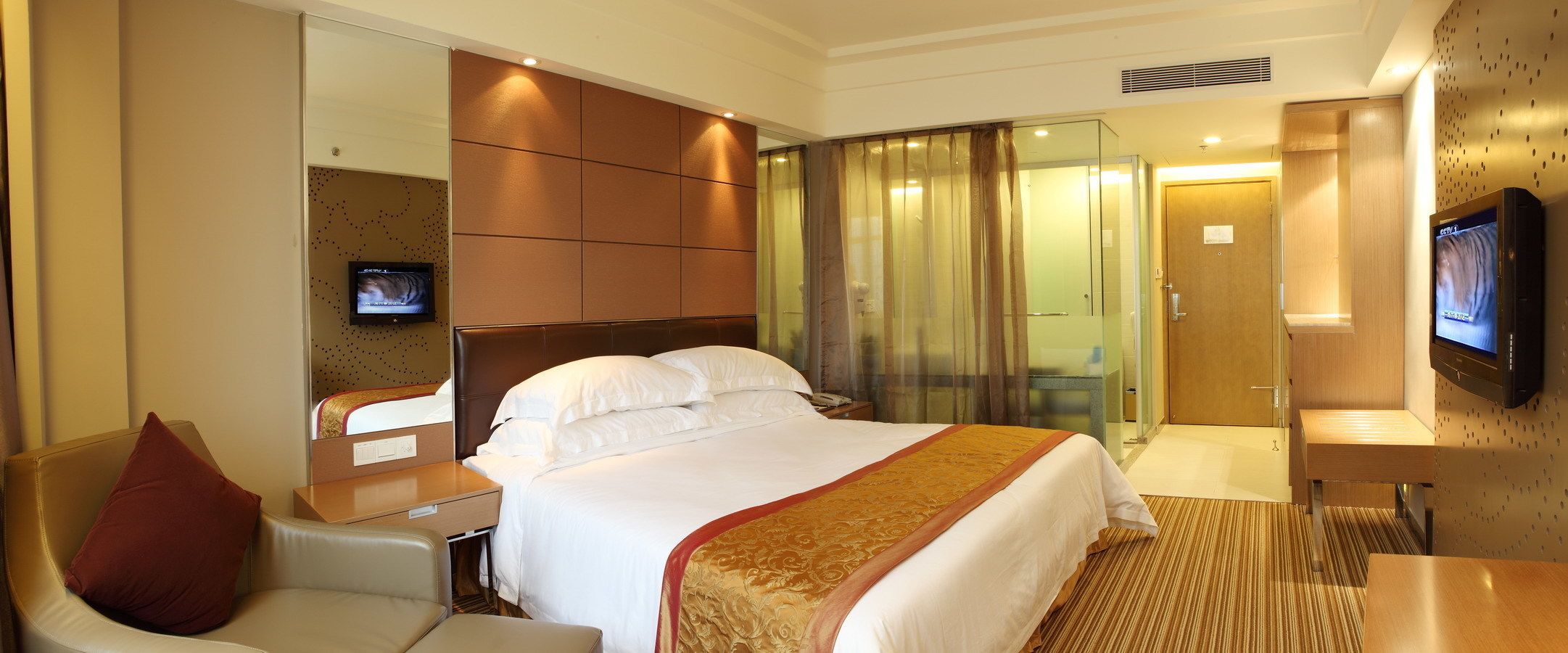 A hotel room with a large bed, a desk, a chair, a television, and a glass partition.
