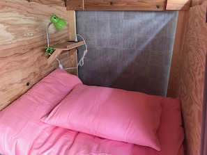 A small wooden room with a bed, a green lamp, and a power outlet. - 81's Inn Hakata - Hostel (Fukuoka)