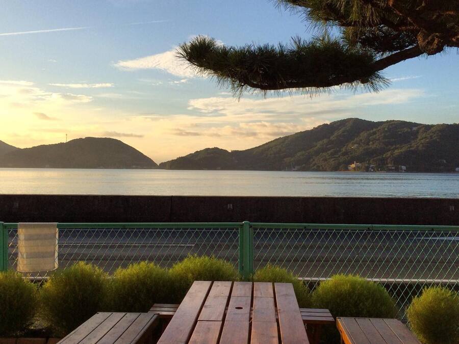 Una terraza de madera con mesas de picnic con vista a un cuerpo de agua y colinas.