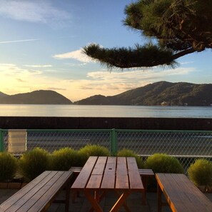 Une terrasse en bois avec des tables de pique-nique, donnant sur un plan d’eau et des collines.