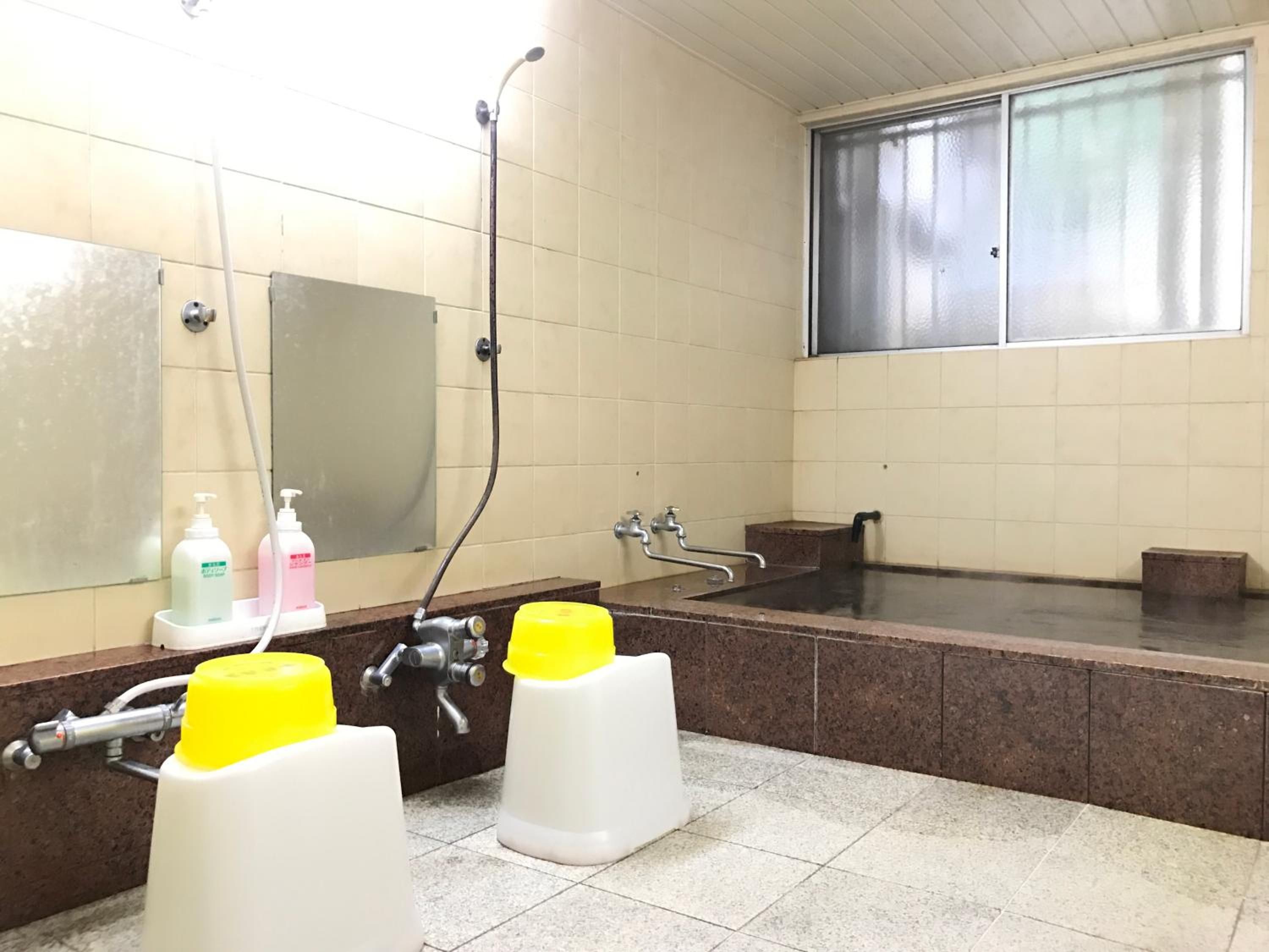 A public restroom with a large mirror, a shower, and two yellow and white soap dispensers.
