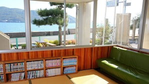 Une bibliothèque dotée de grandes fenêtres, d’étagères en bois, d’un canapé vert et offrant une vue sur un lac et des montagnes.