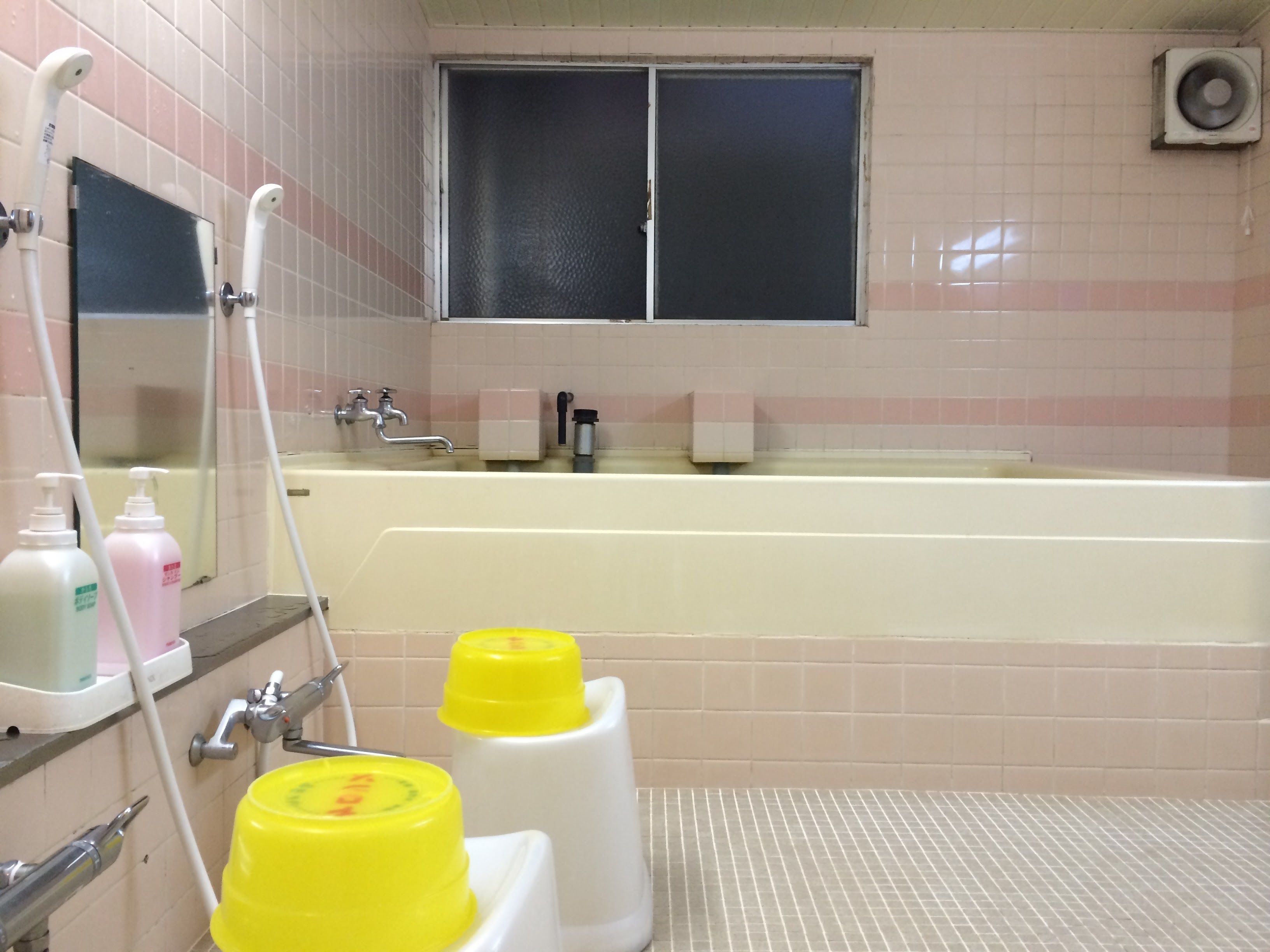 A bathroom with a bathtub, a mirror, a window, and toiletries on the counter.
