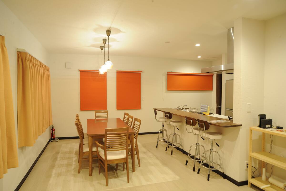 A compact kitchen with a refrigerator, a sink, and a bar area. There is a dining table with chairs and a ceiling light fixture.