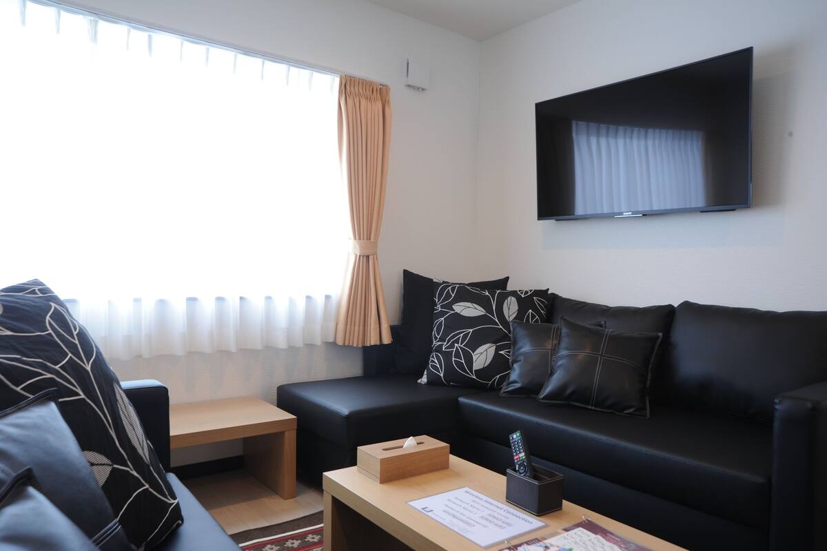 A modern living room with a black leather sofa, a wooden coffee table, and a flat-screen TV mounted on the wall.
