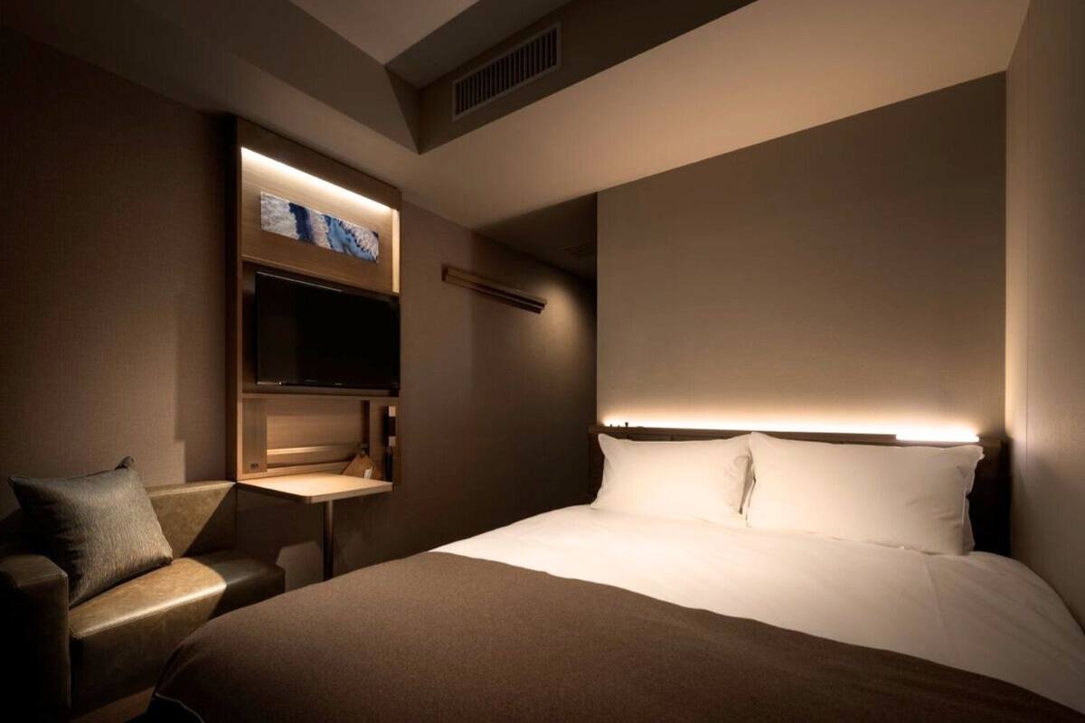 A modern hotel room with a large bed, a flat-screen TV mounted on the wall, and a small desk with a chair.