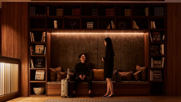 A cozy seating area with a sofa and a bench, surrounded by wooden bookshelves filled with books and decorative items. - Nest Hotel Tokyo Hanzomon (Tokyo)
