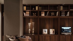 A modern living room with a built-in wooden bookshelf, a flat-screen TV, and a leather sofa. - Nest Hotel Tokyo Hanzomon (Tokyo)