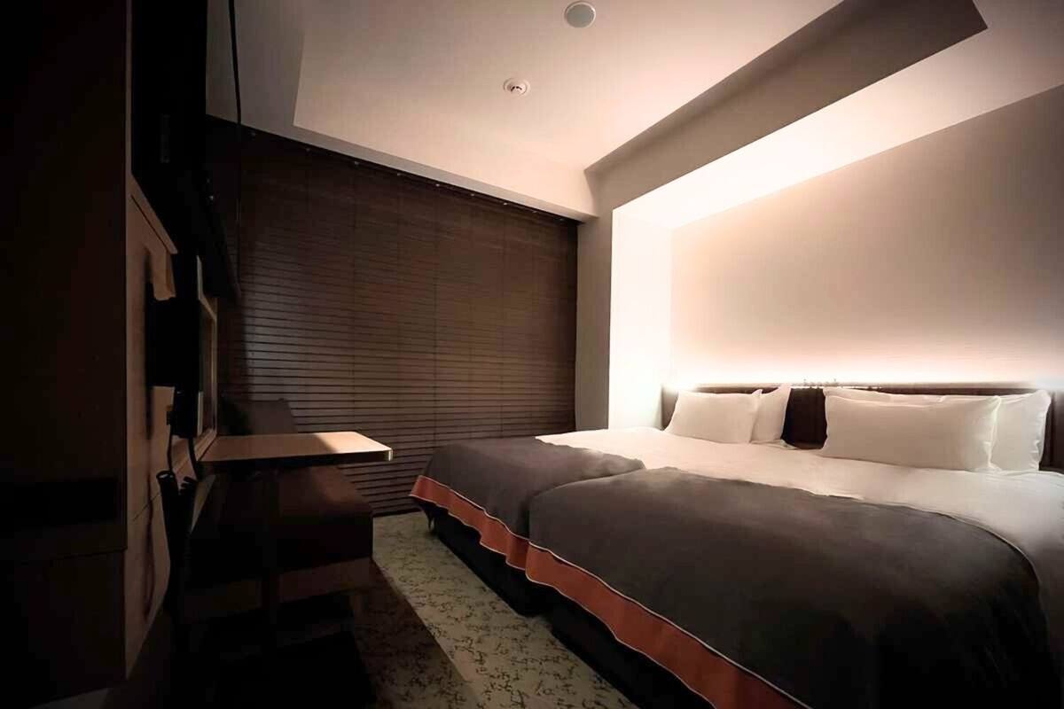A modern bedroom with a large bed, a nightstand, a dresser, and a window with blinds.