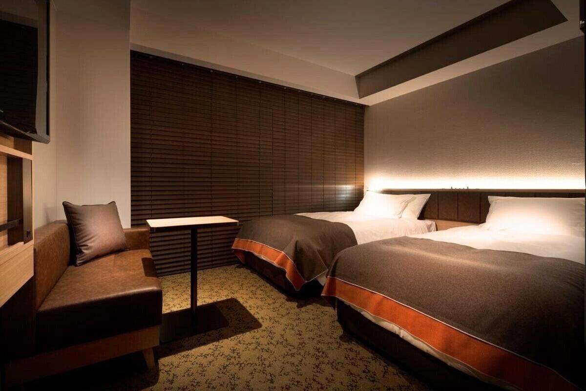 A hotel room with two beds, a sofa, a small table, and a TV.