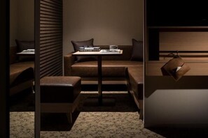 A modern, dimly lit room with a sofa, a small table, and a hanging bag. - Nest Hotel Tokyo Hanzomon (Tokyo)