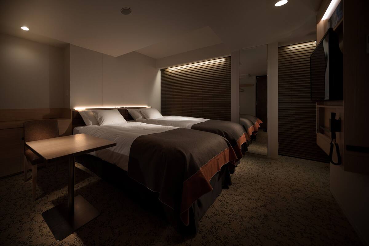 A modern hotel room with a large bed, bedside tables, a desk, and a walk-in closet.