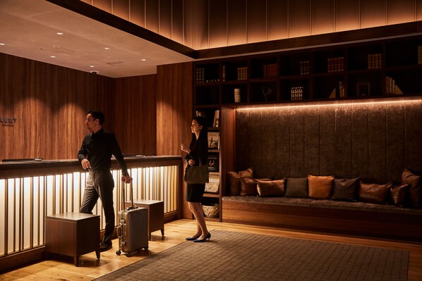 A reception area with a wooden reception desk, a seating area with a sofa, and a bookshelf with various items. - Nest Hotel Tokyo Hanzomon (Tokyo)