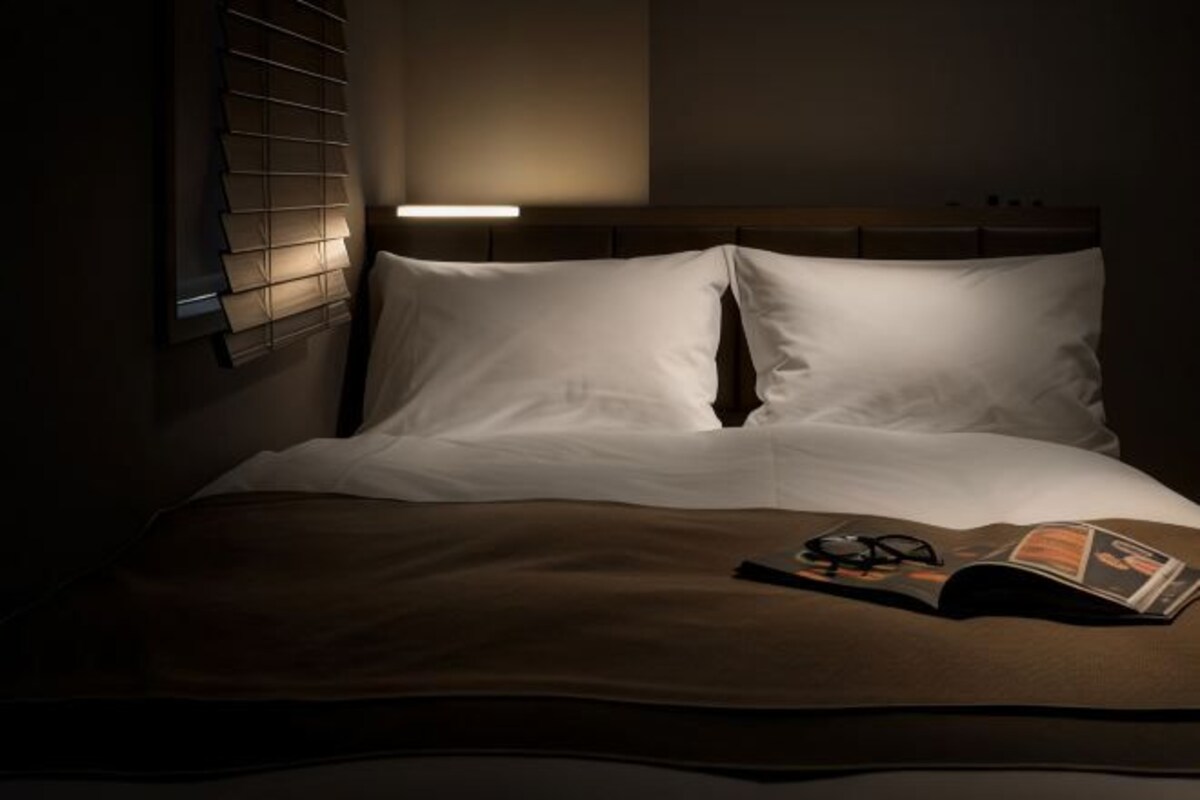 A neatly made bed with white linens, a brown throw blanket, and a magazine with glasses on it.