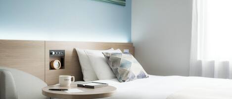 Una habitación de hotel moderna con una cama bien hecha, una mesita de noche con una taza de café, un control remoto y un reloj de pared.
