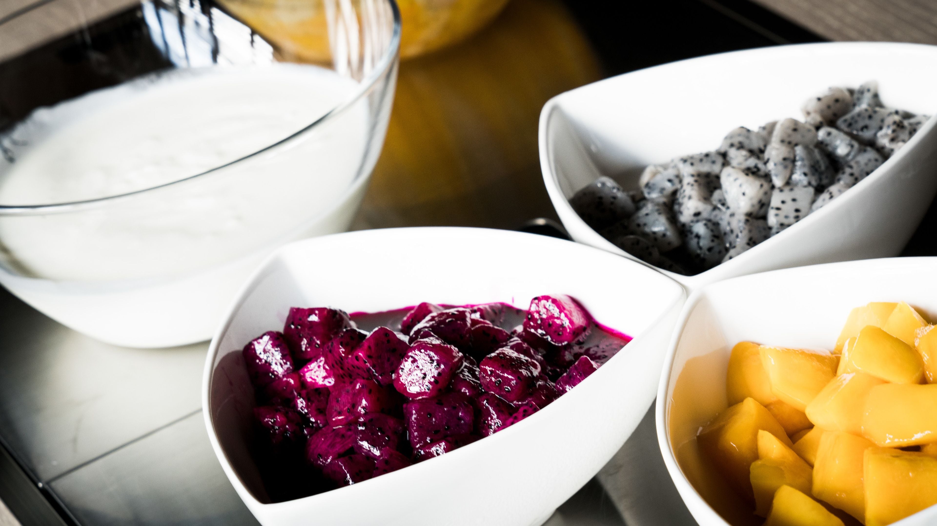 Four bowls of different fruits and a bowl of white liquid on a table.