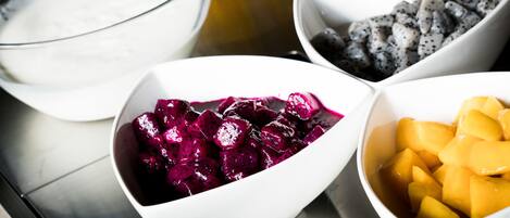 Four bowls of different fruits and a bowl of white liquid on a table.