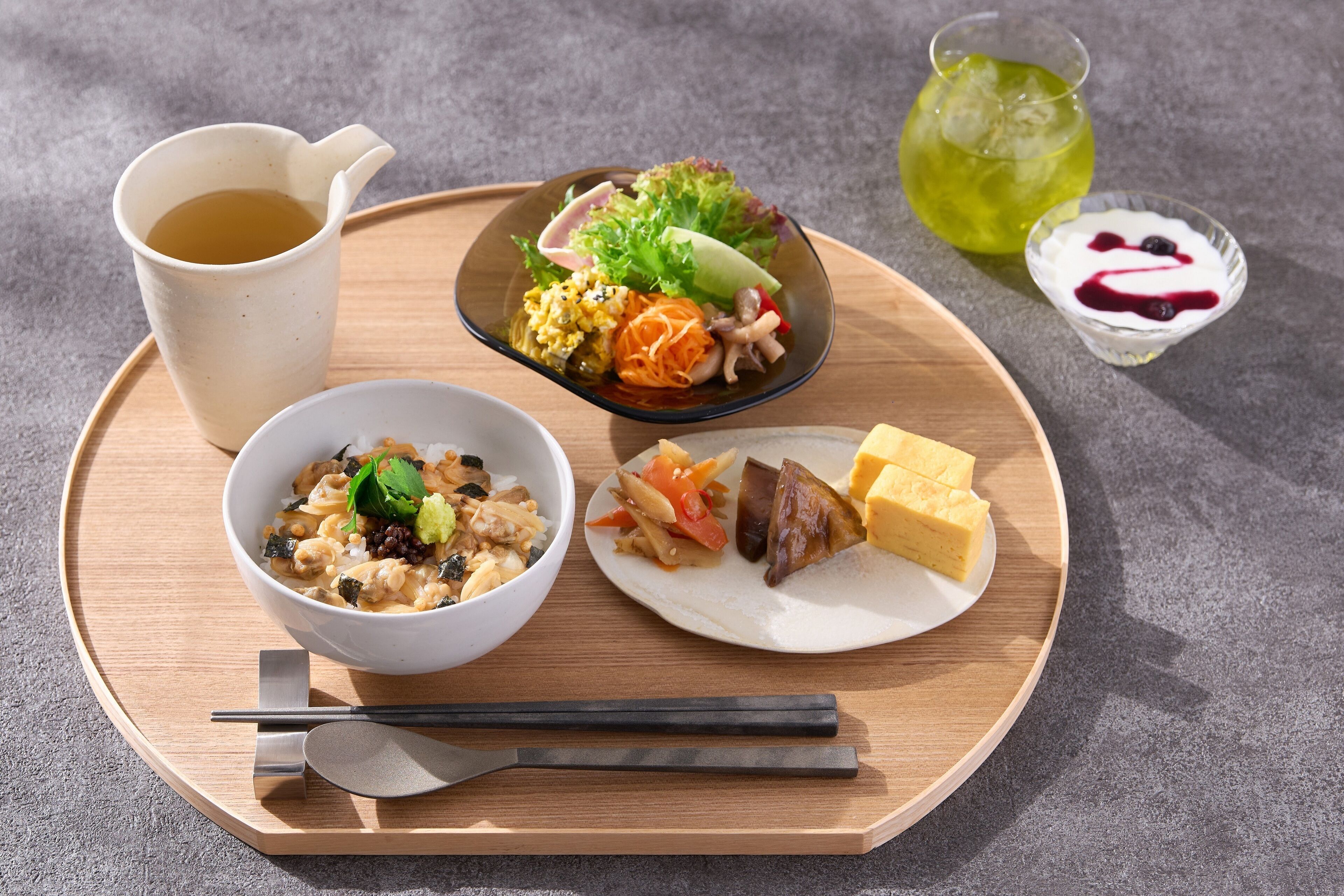 Un plateau en bois avec un bol de riz, une assiette de viande et de légumes, un petit bol de salade, une tasse de thé et un verre de boisson verte.