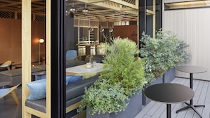 Un intérieur moderne agrémenté de poutres en bois, de coins salon et d’une petite table sur laquelle est posé un pot de fleurs.