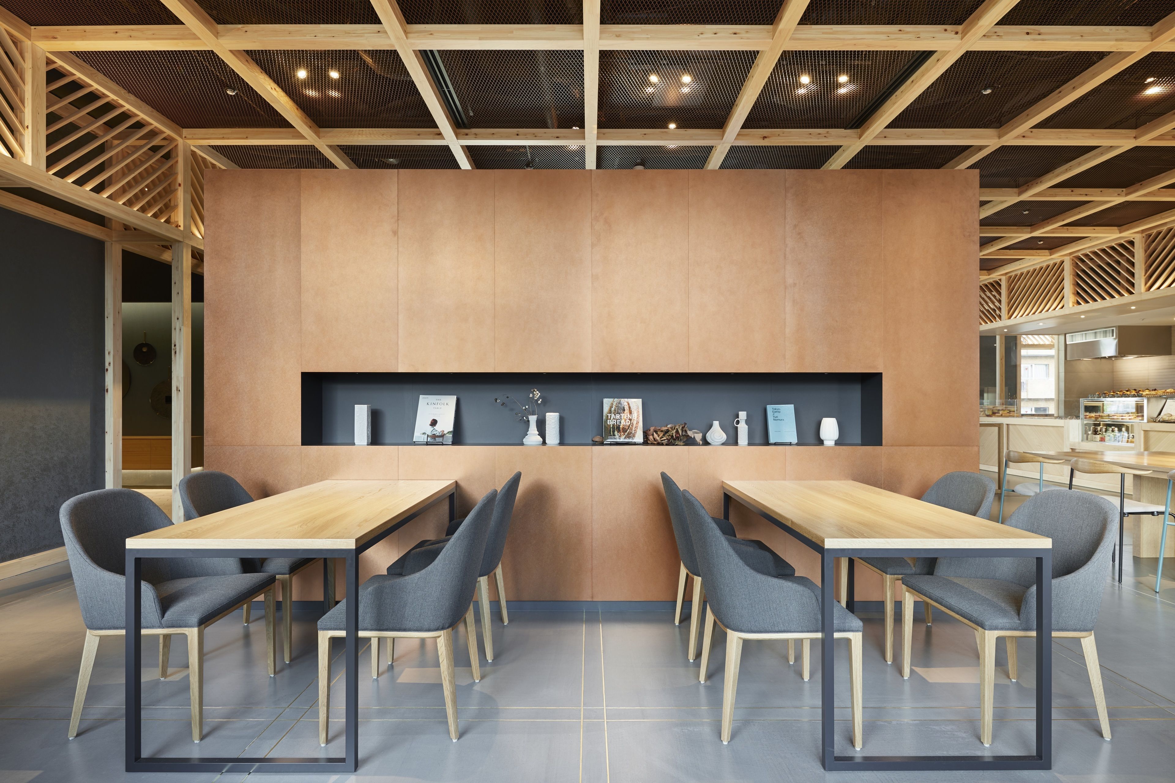 A modern conference room with a wooden table and chairs, a central display, and a kitchen area in the background.