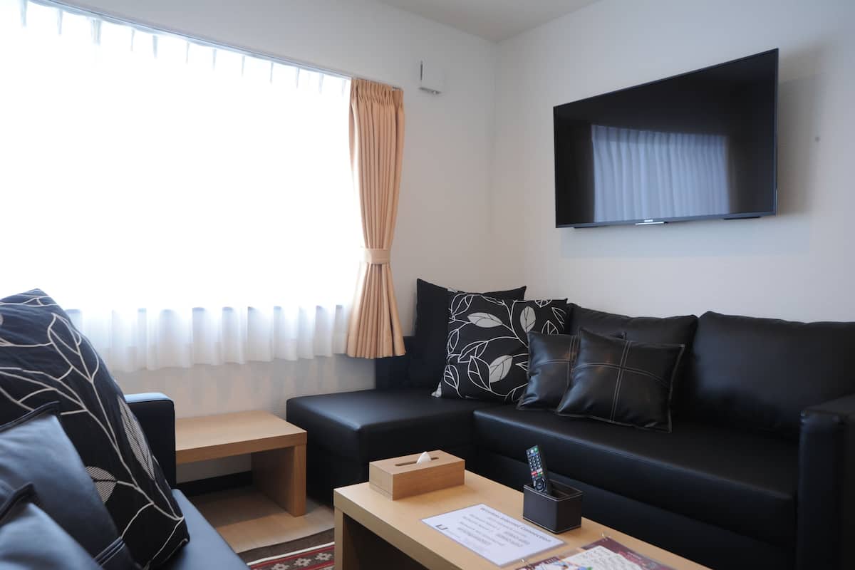 A modern living room with a black leather sofa, a wooden coffee table, and a flat-screen TV mounted on the wall.